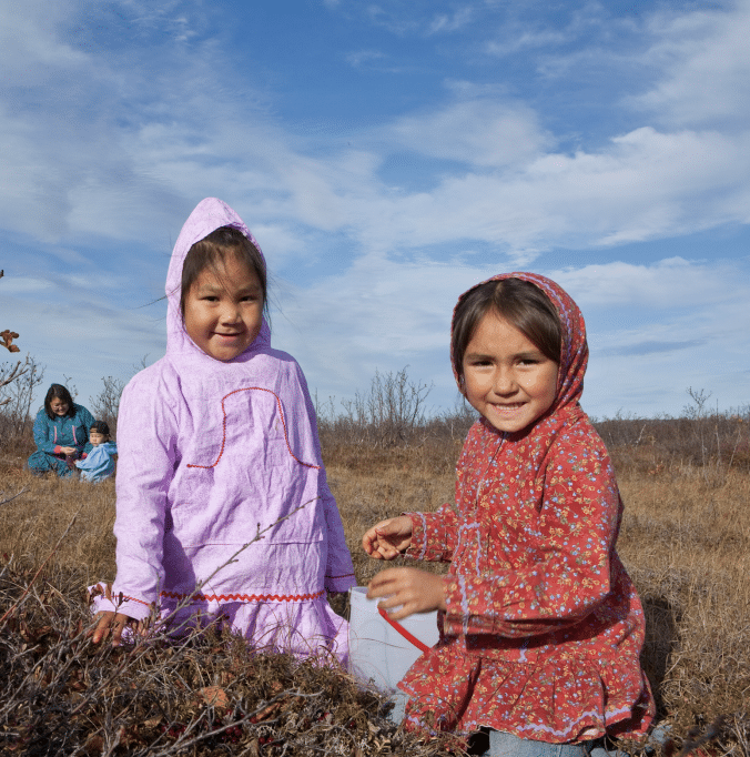 Two little girls pick berries on the tundra.